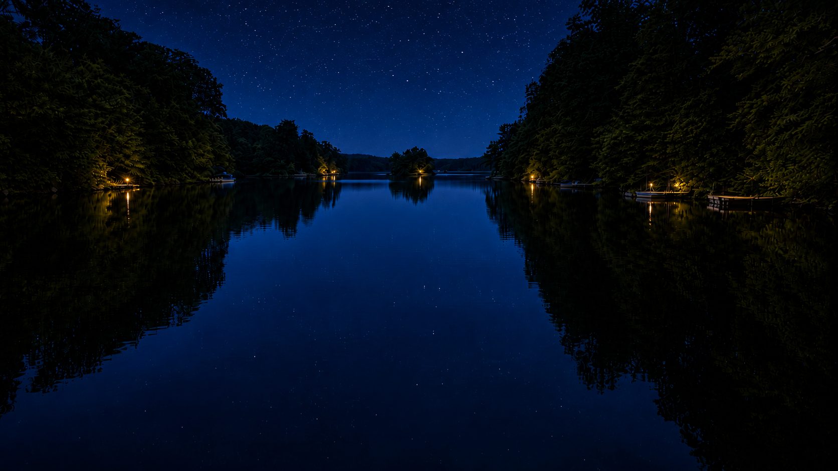 The lake at night under a starry sky with cabin lights on the far shore