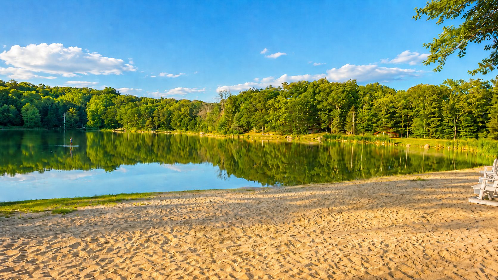 Sandy lake beach with white chairs on a summer day